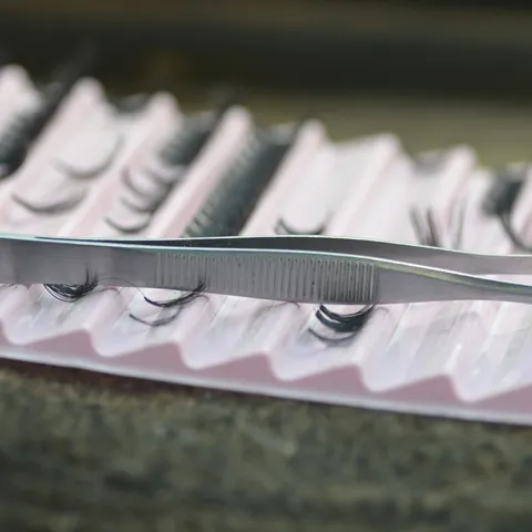 Steel tweezers resting on a pink tray of lash strips