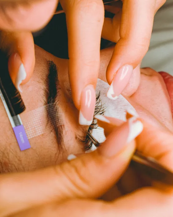 An artist in gloves working on a client's brow with a brow pencil and tweezers