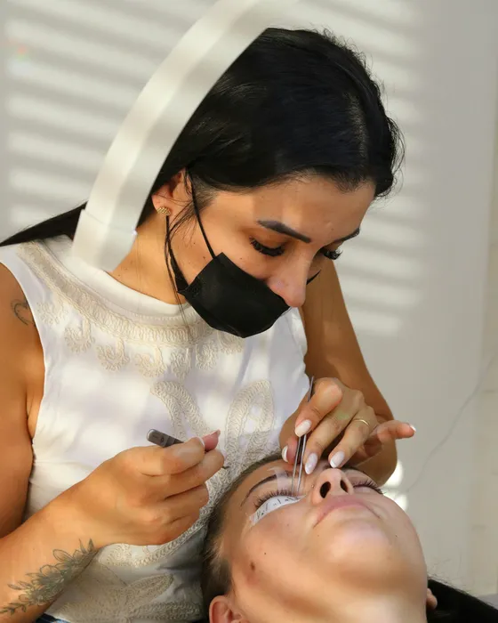 An artist in a face mask working on a client's lashes in a bright studio