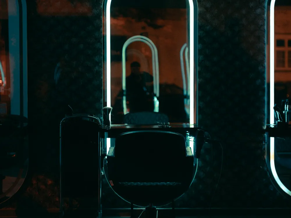 A black styling chair in front of an arched mirror lit with neon