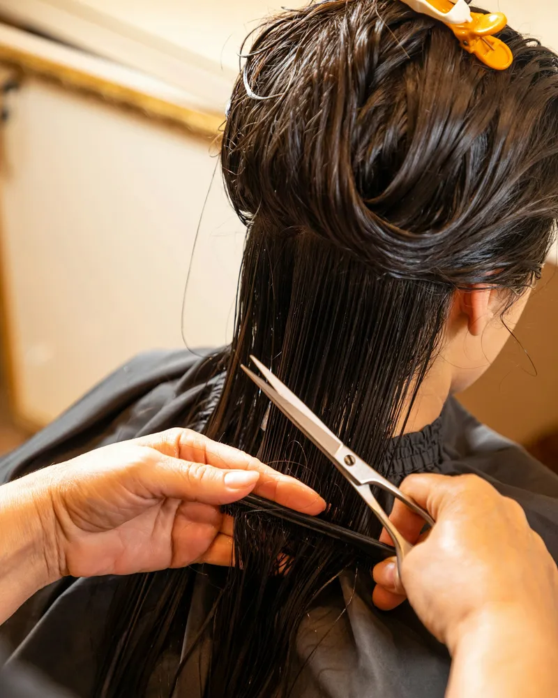 Shears cutting a straight line through long dark hair held between fingers