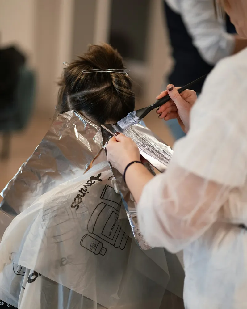 A stylist placing foils in a client's hair, seen from behind