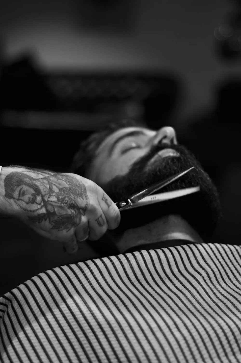 Black and white photo of a barber trimming a full beard with scissors