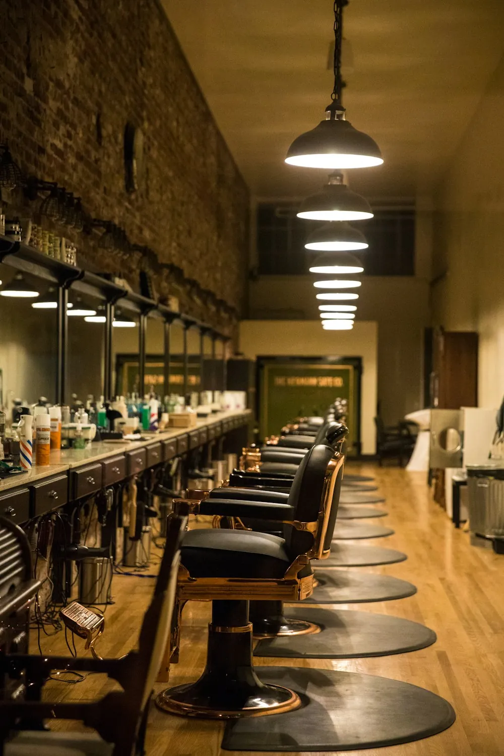 A long, empty shop floor with a row of barber chairs and pendant lamps