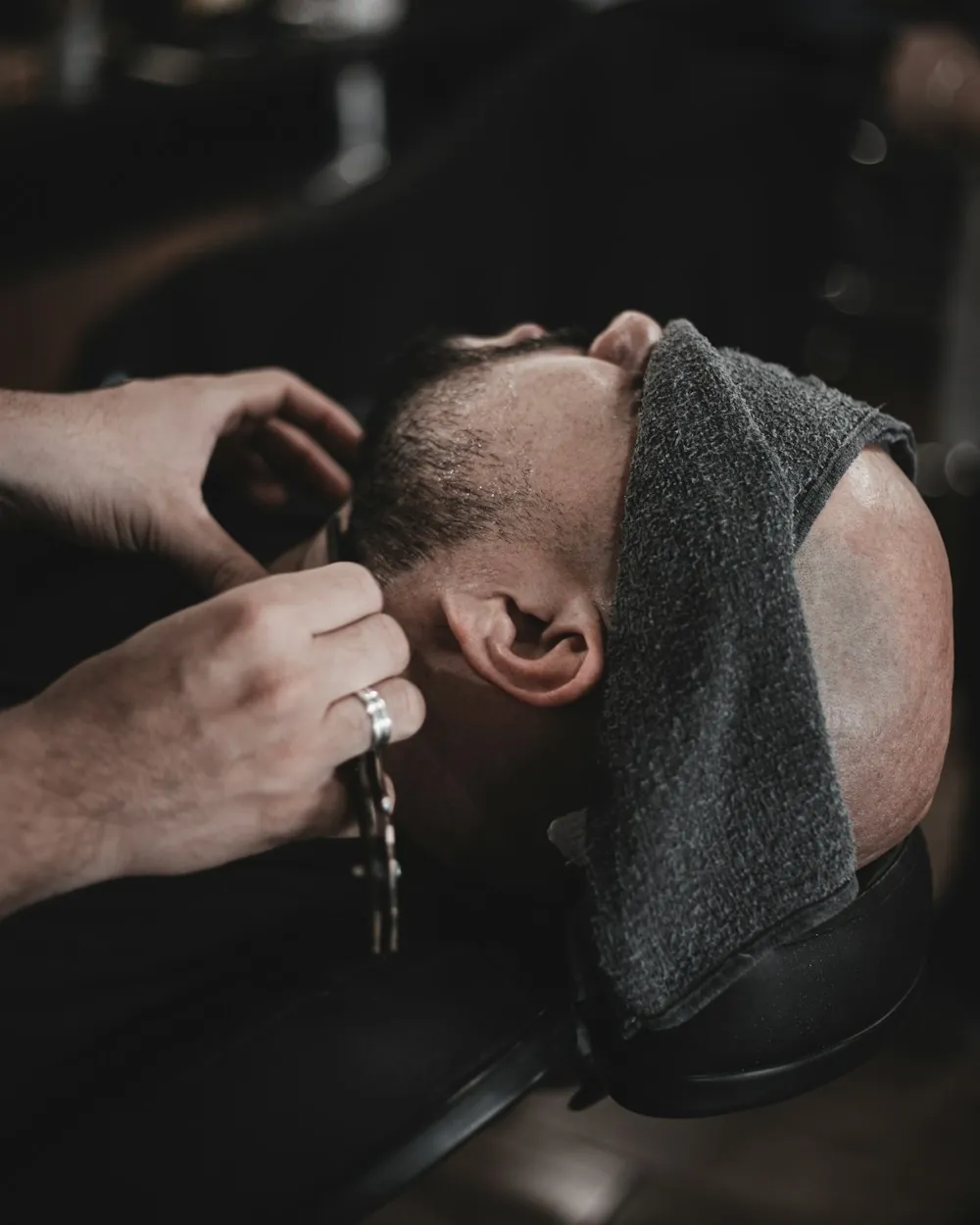 A reclined client under a towel while the barber works a straight razor along his jaw