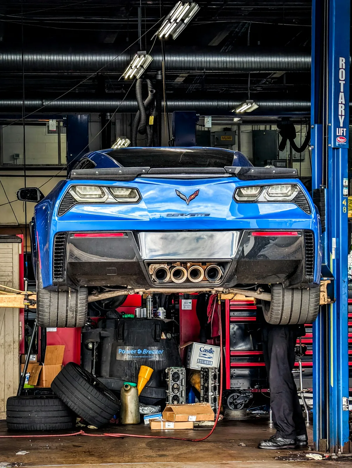 A blue sports car raised on a two post lift in the service bay