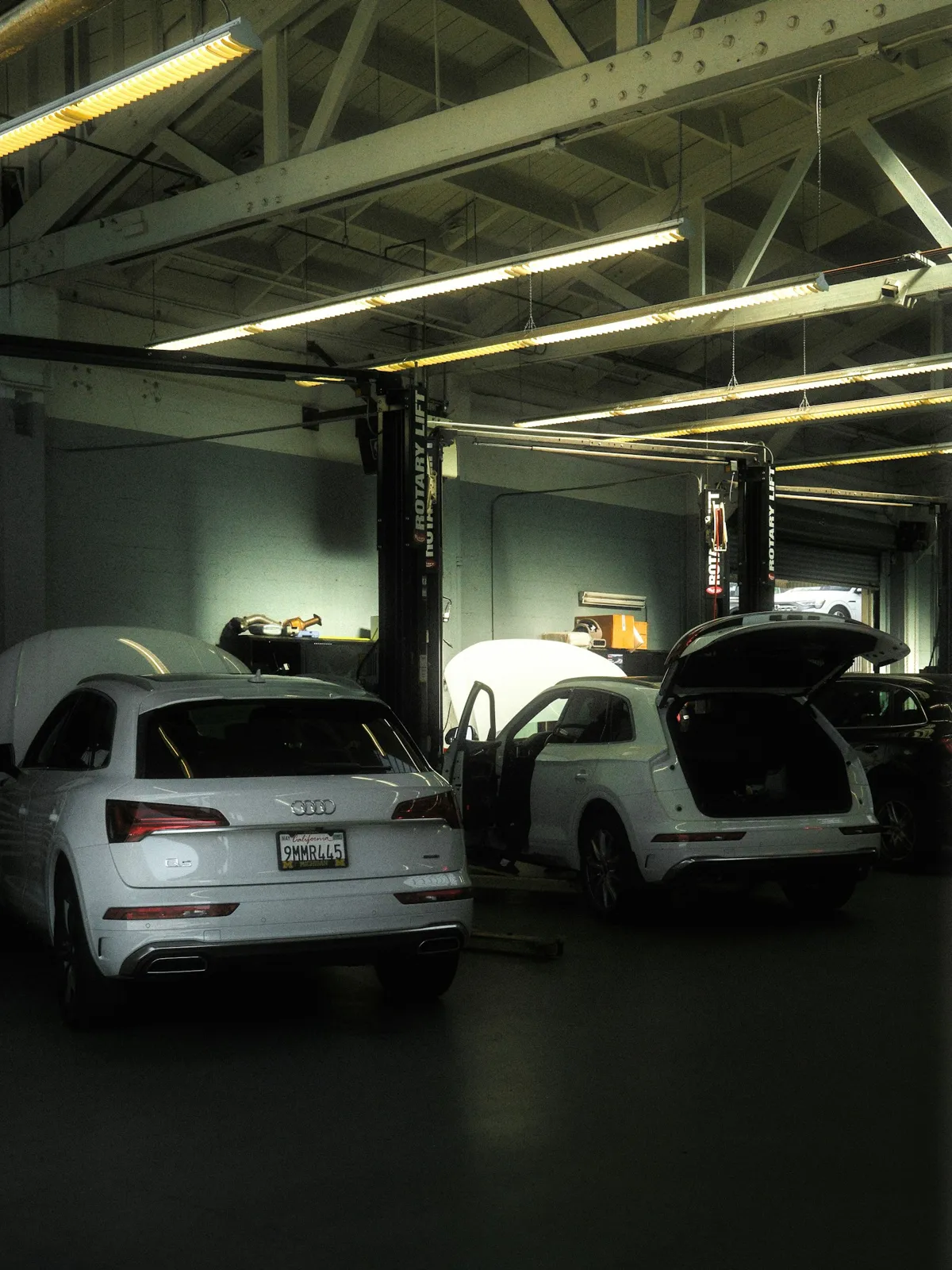 Two white SUVs on lifts in a brightly lit service bay