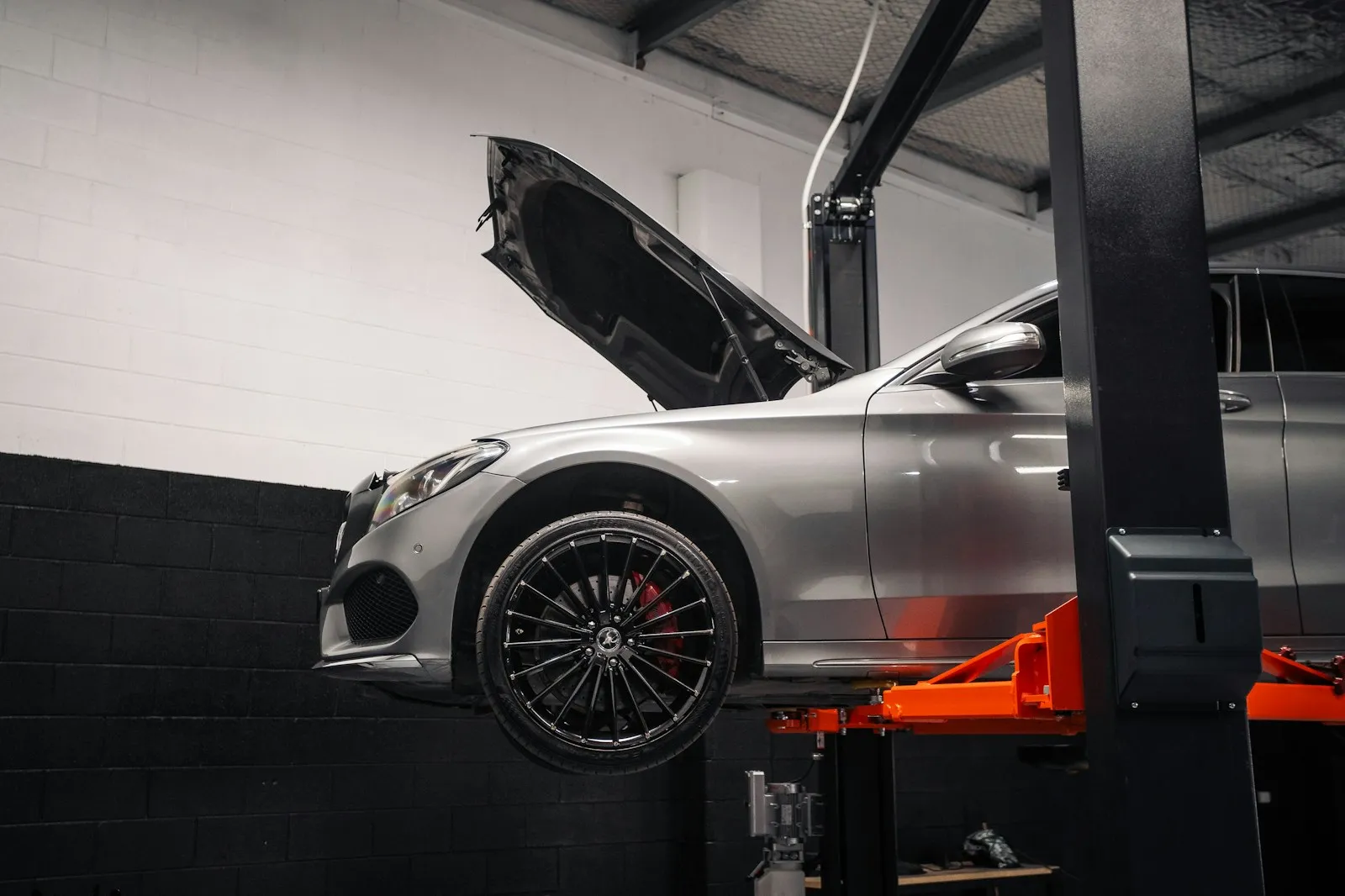 A silver car with its hood open, raised on a lift in the service bay