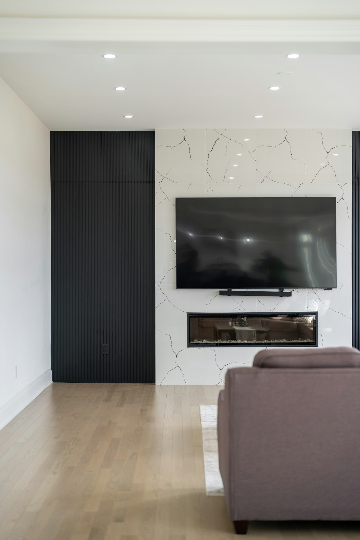 Marble feature wall with a mounted TV, linear electric fireplace and a dark slat panel beside it