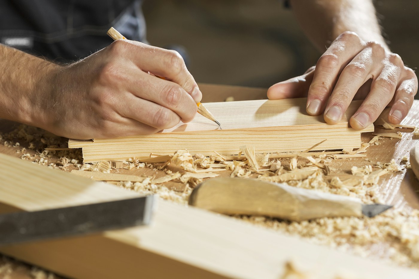 Hands marking a cut line on a wood board with a pencil