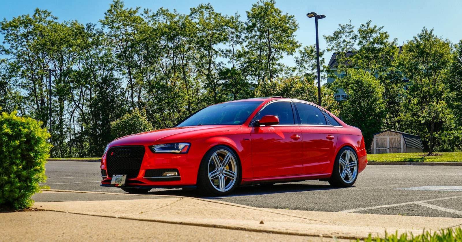 Red sedan with tinted windows parked by green trees