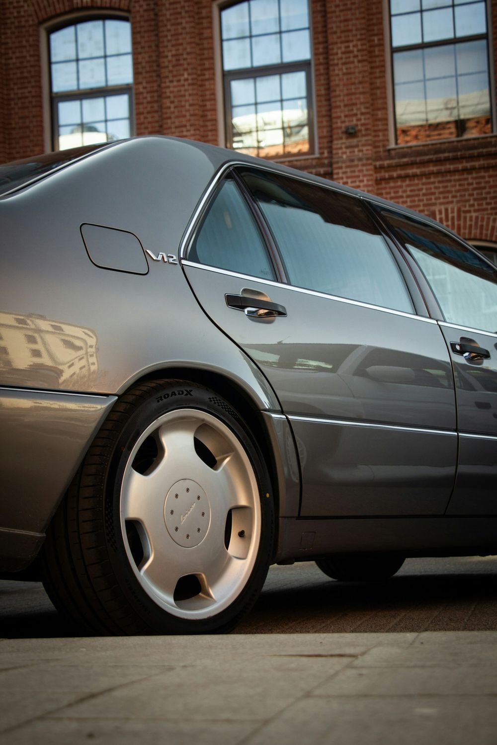Gray luxury sedan with tinted windows beside a brick building